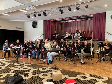 A group of people sitting in chairs in a room with a stage and a curtain

Description automatically generated